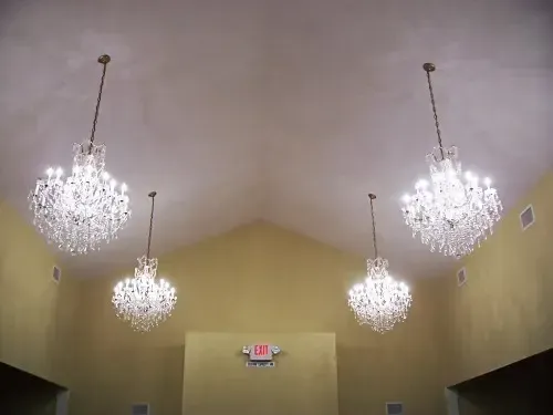 three chandeliers are hanging from the ceiling in a room with an exit sign .