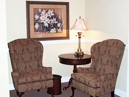 two chairs and a table in a living room with a picture on the wall above them .