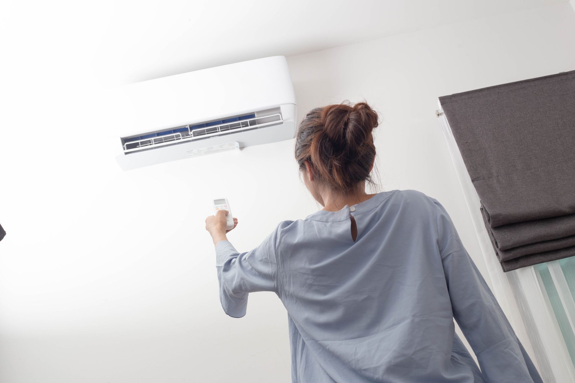 A woman is adjusting her air conditioner with a remote control.