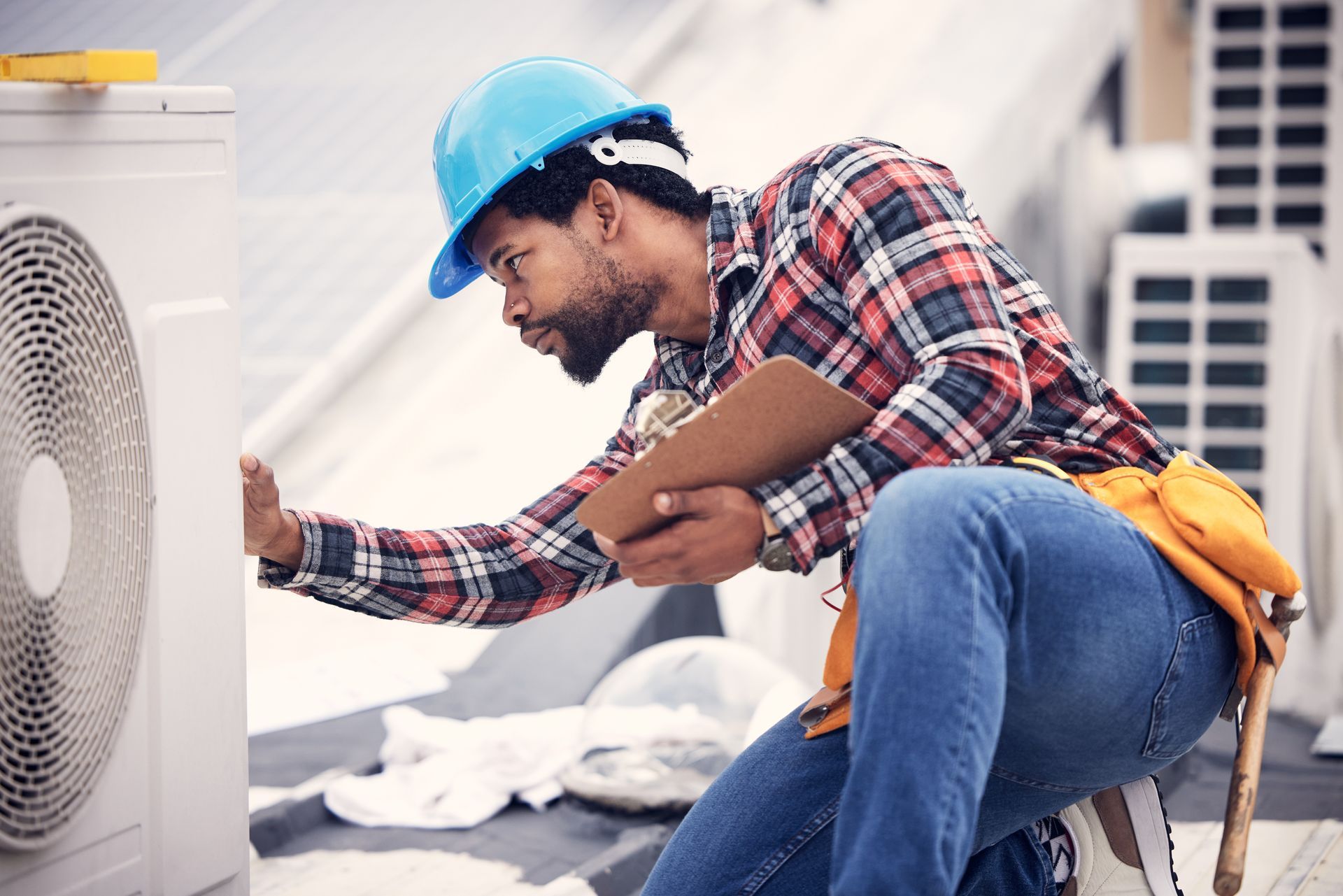A man wearing a hard hat is working on an air conditioner.