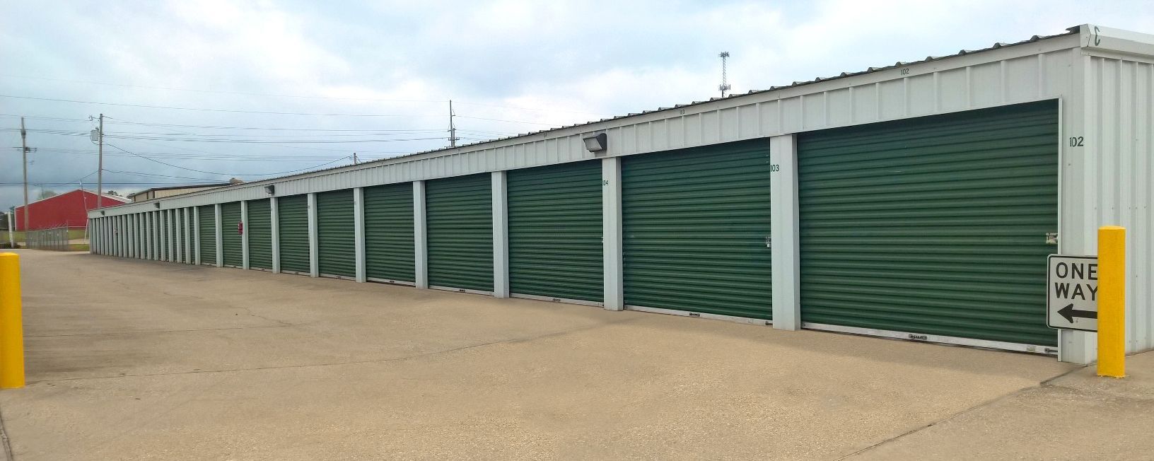 A row of storage units with green doors are lined up in a parking lot. A row of storage units with green doors are lined up in a parking lot.