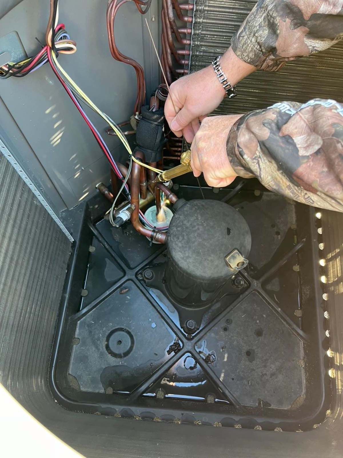 A person is working on an air conditioner with a pair of pliers.