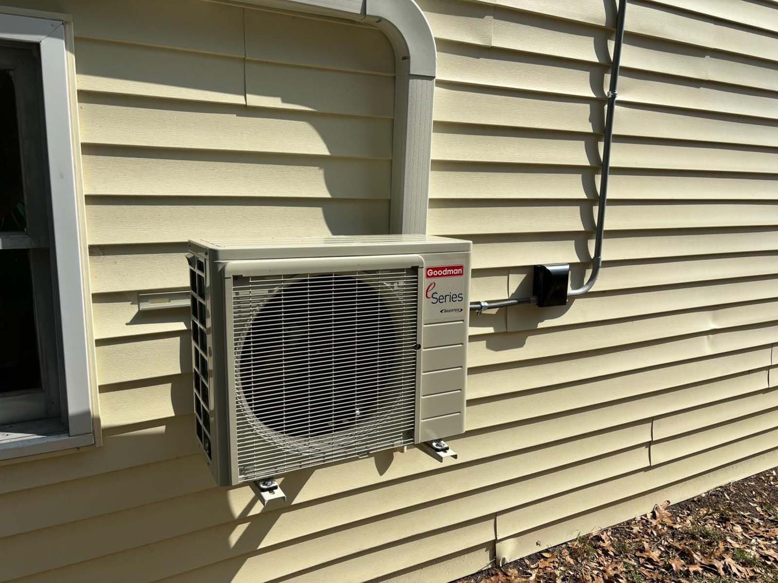 An air conditioner is mounted on the side of a house next to a window.