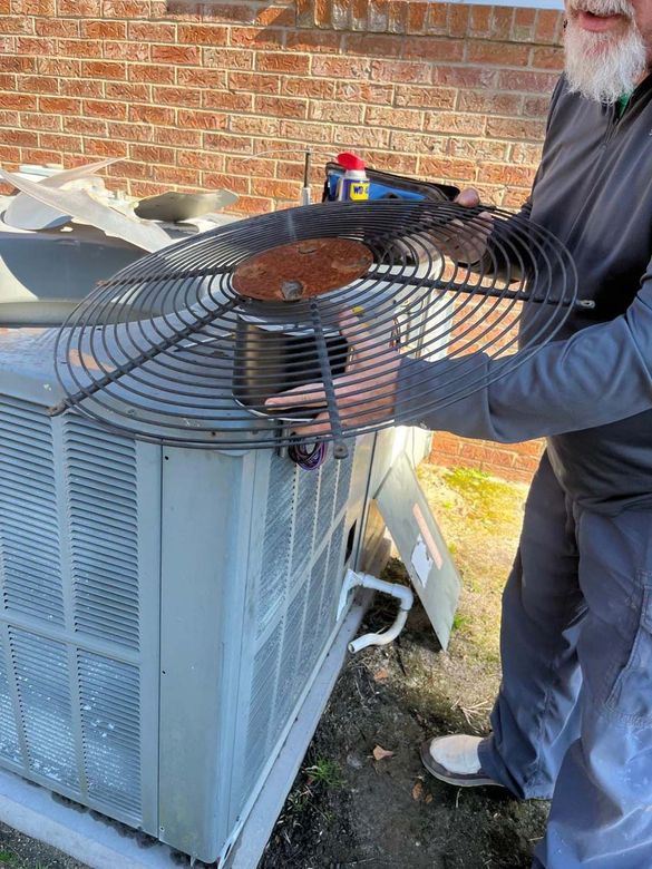 A man is working on an air conditioner outside of a brick building.