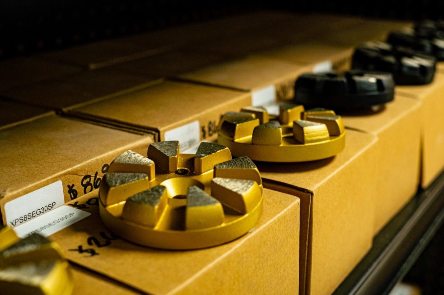 Gold ribbon spools lined up on stacked cardboard boxes in a warehouse setting
