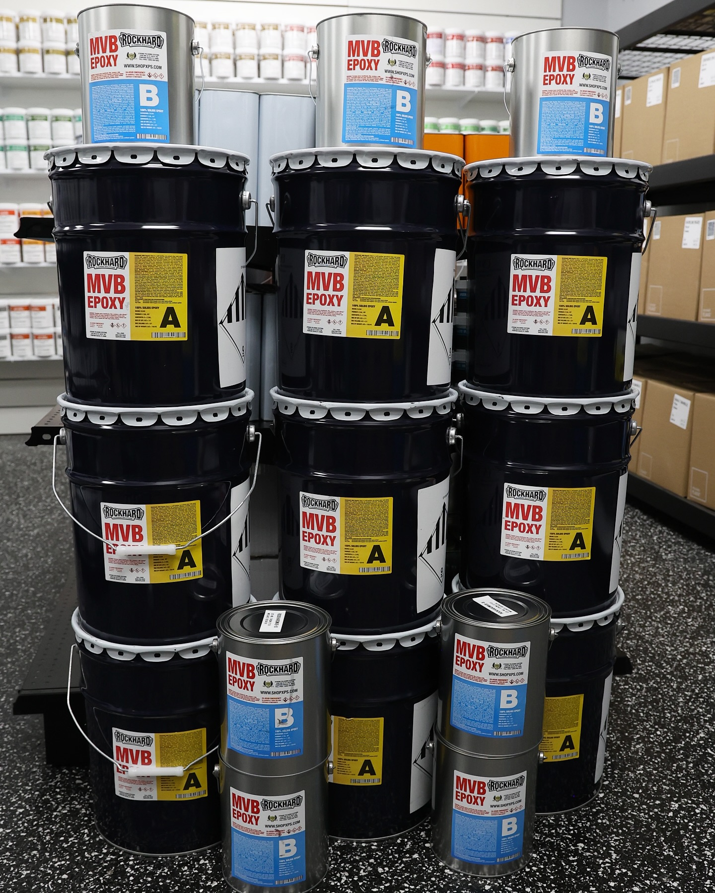 Stacked black industrial drums with red-and-white labels in a warehouse aisle.