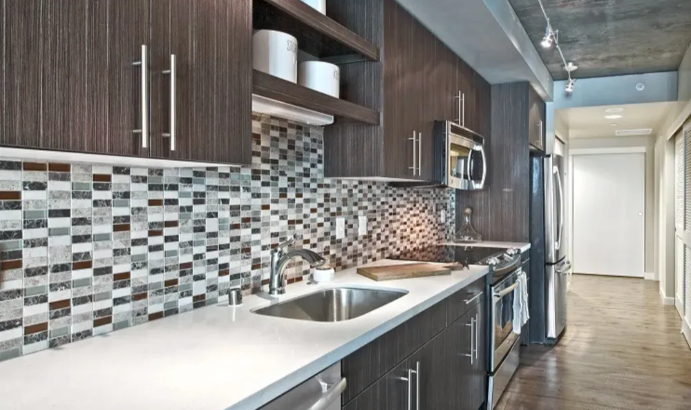 Modern apartment kitchen with dark wood cabinets, stainless appliances, and mosaic tile backsplash.