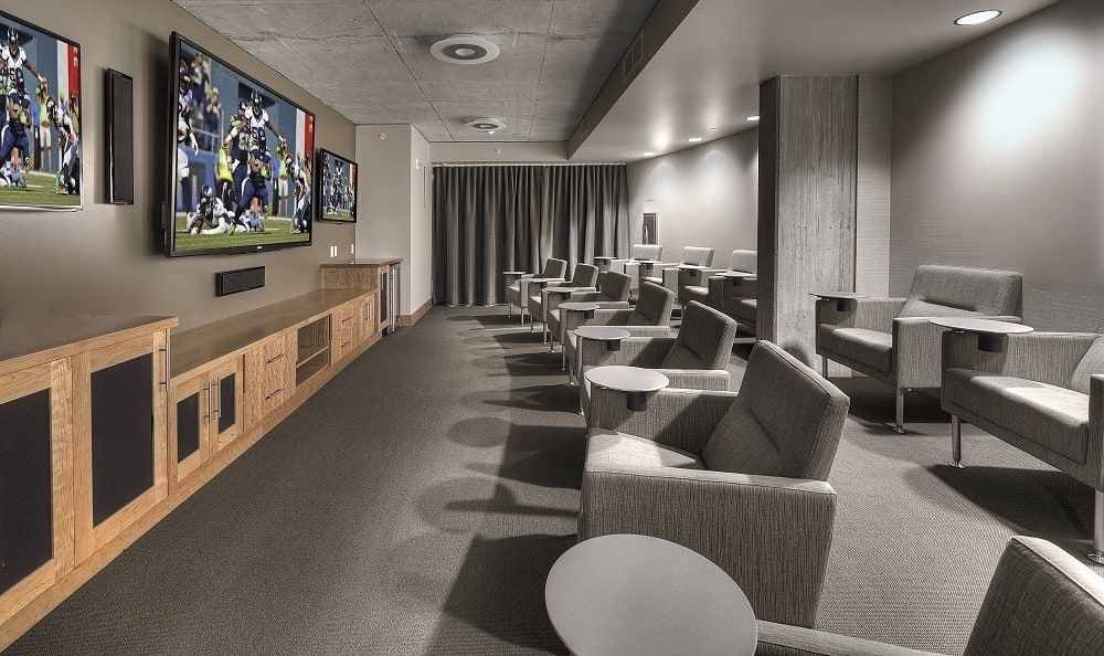 Indoor resident lounge with gray seating facing wall-mounted TVs and a wooden cabinet.