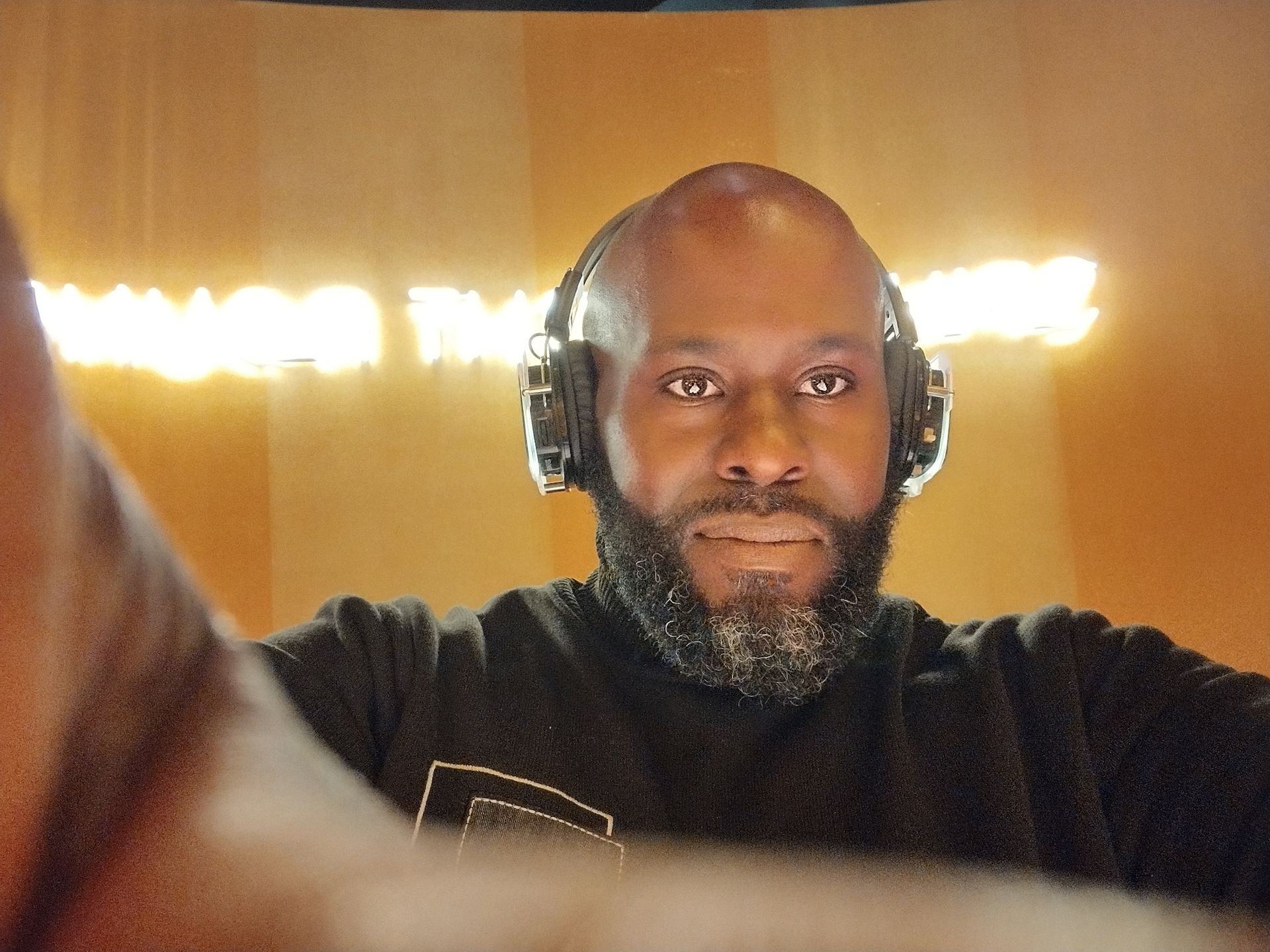 A person with a beard and headphones poses for a selfie in a warm-lit, dimly lit setting.