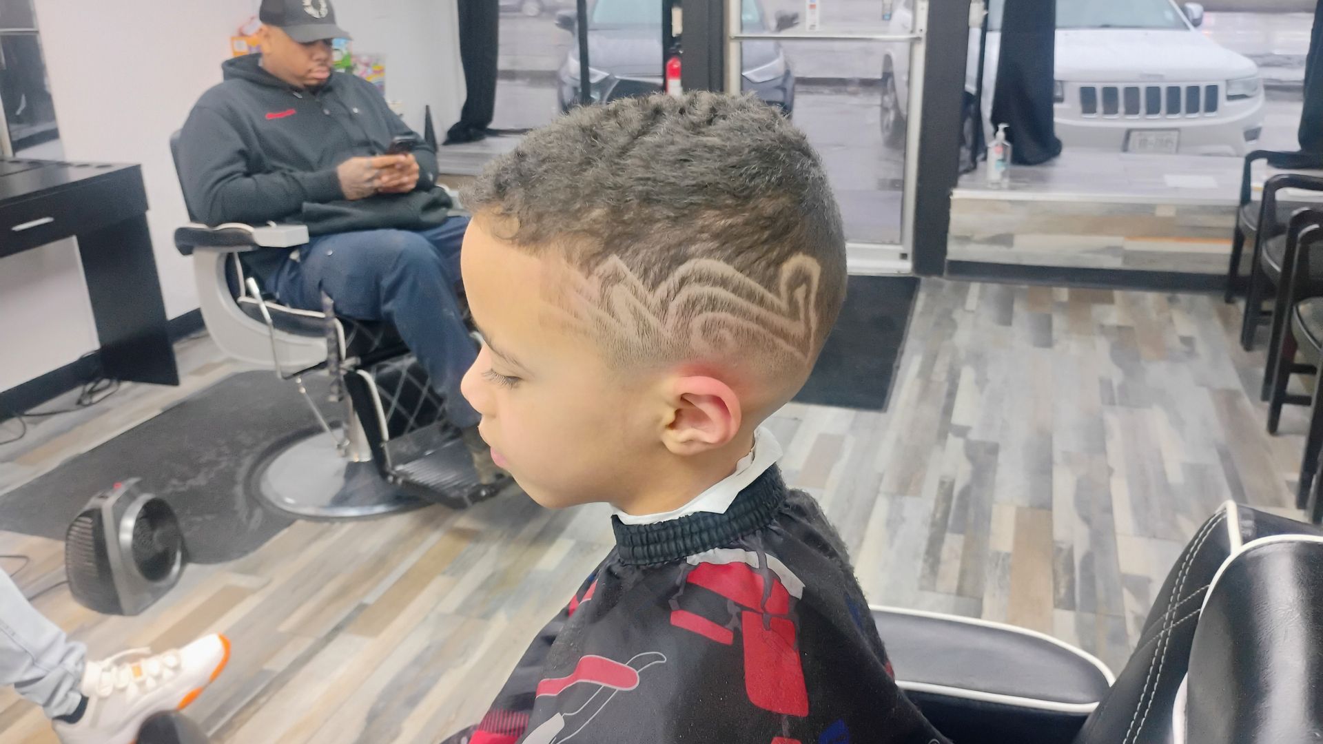 A barber shop scene with a person in a salon cape featuring a detailed, wave-like hair design shaved into the side.