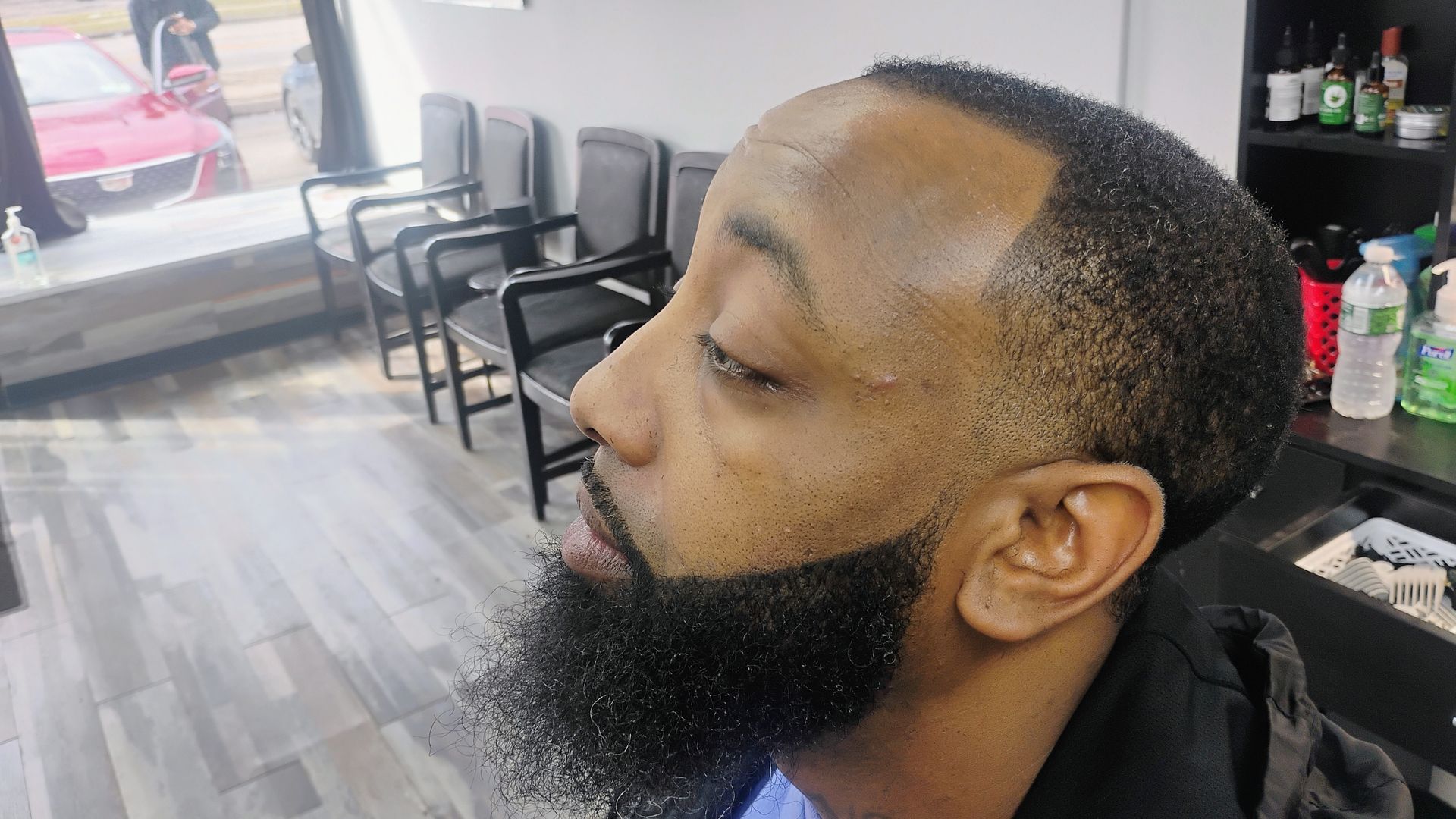A profile shot of a man with a fresh haircut and neatly trimmed beard in a barbershop.