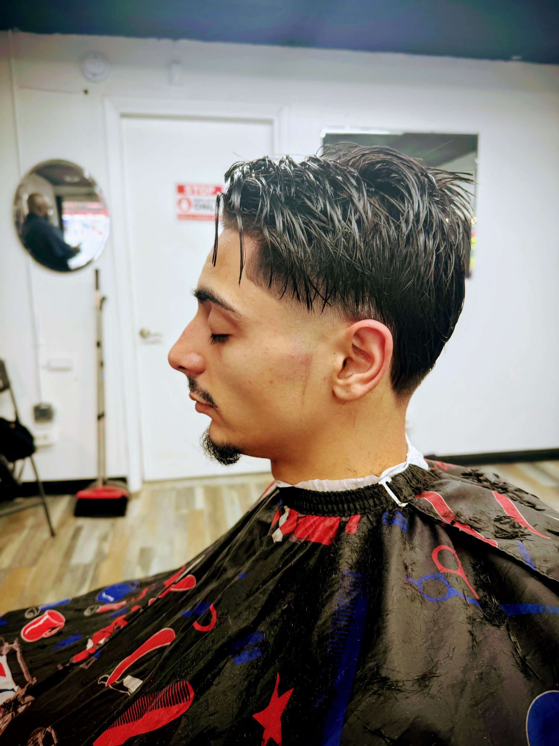 A profile view of a person wearing a barber cape in a salon, showcasing a fresh taper fade haircut with textured top.