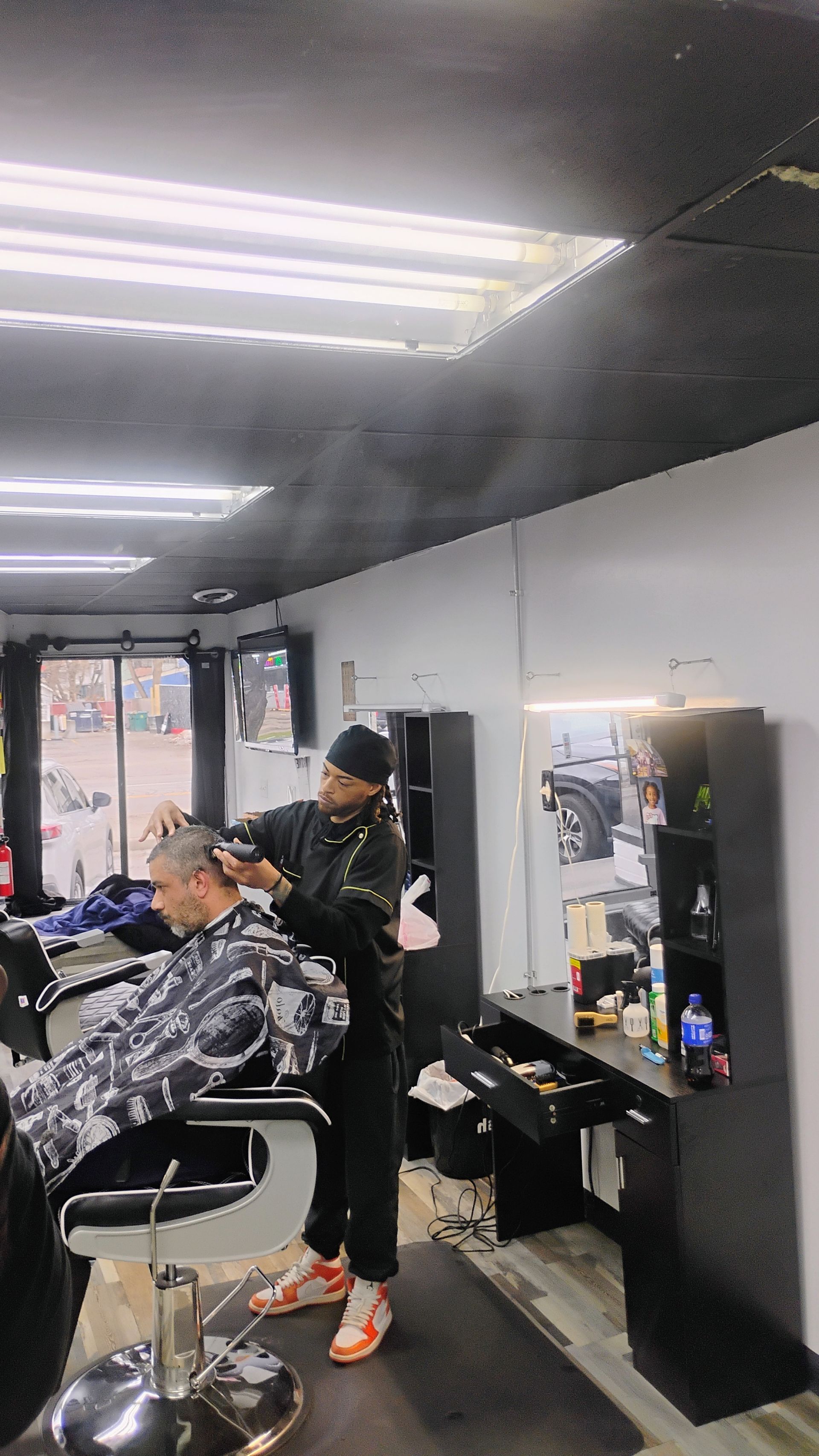 A barber cuts a client's hair using clippers inside a brightly lit, professional barbershop.