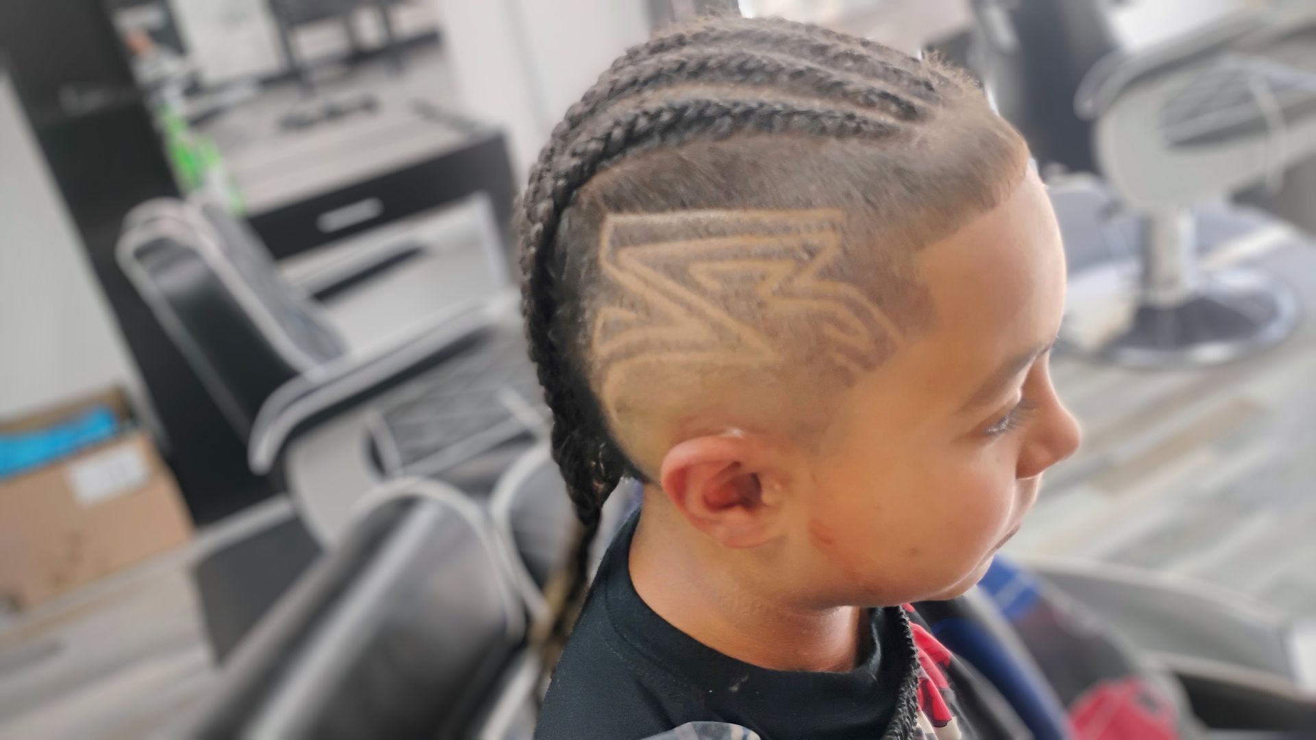 A person with cornrows and a shaved side featuring a lightning bolt design in a barbershop.