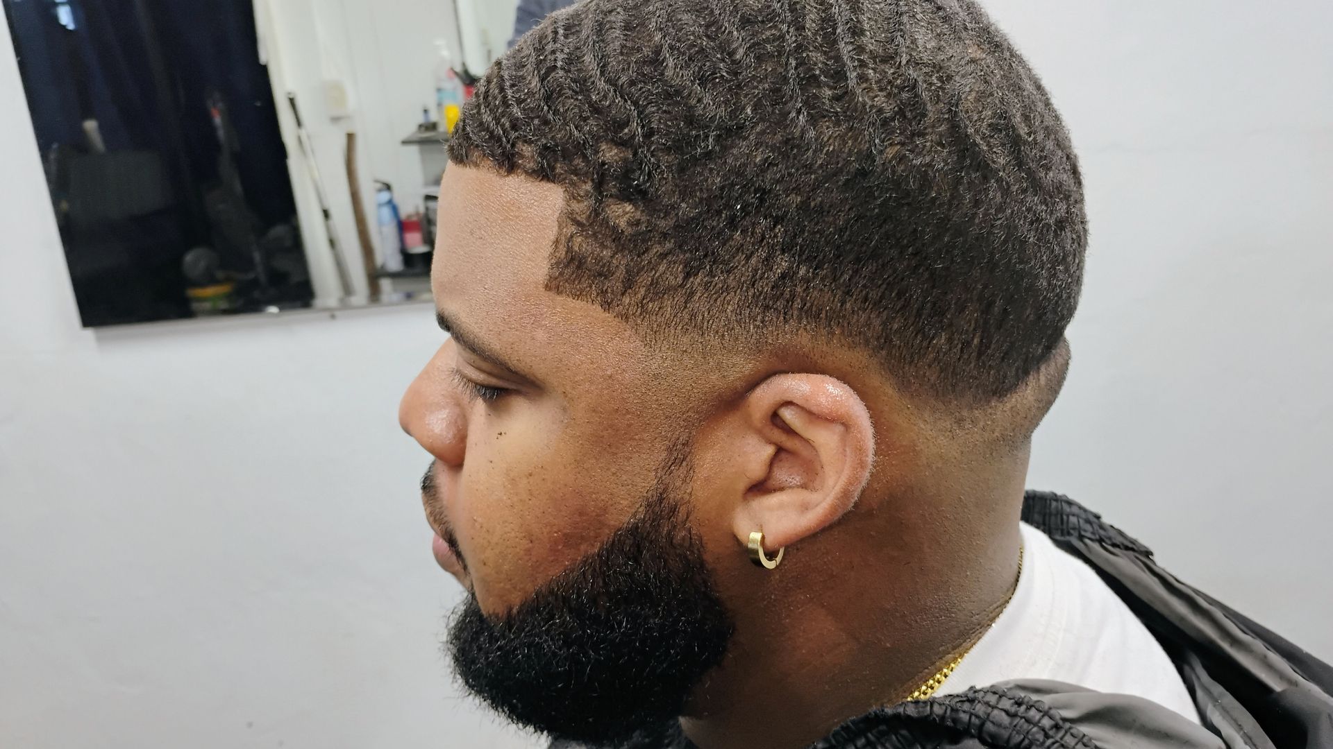 A close-up profile view of a person with a precision fade haircut and a groomed beard.