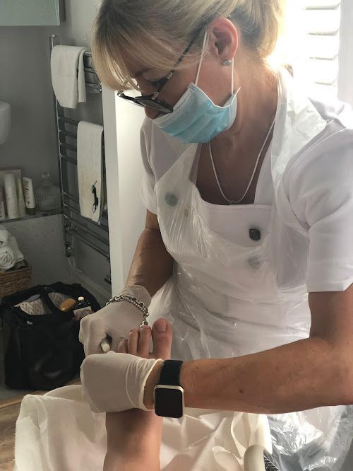 A woman wearing a mask and gloves is working on a person 's feet.