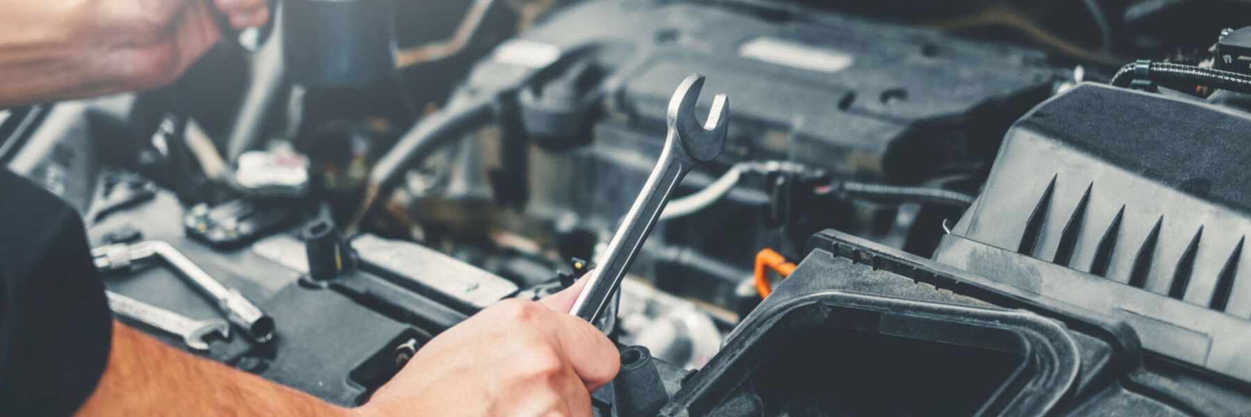 A man is working on a car engine with a wrench | German Auto of Santa Maria