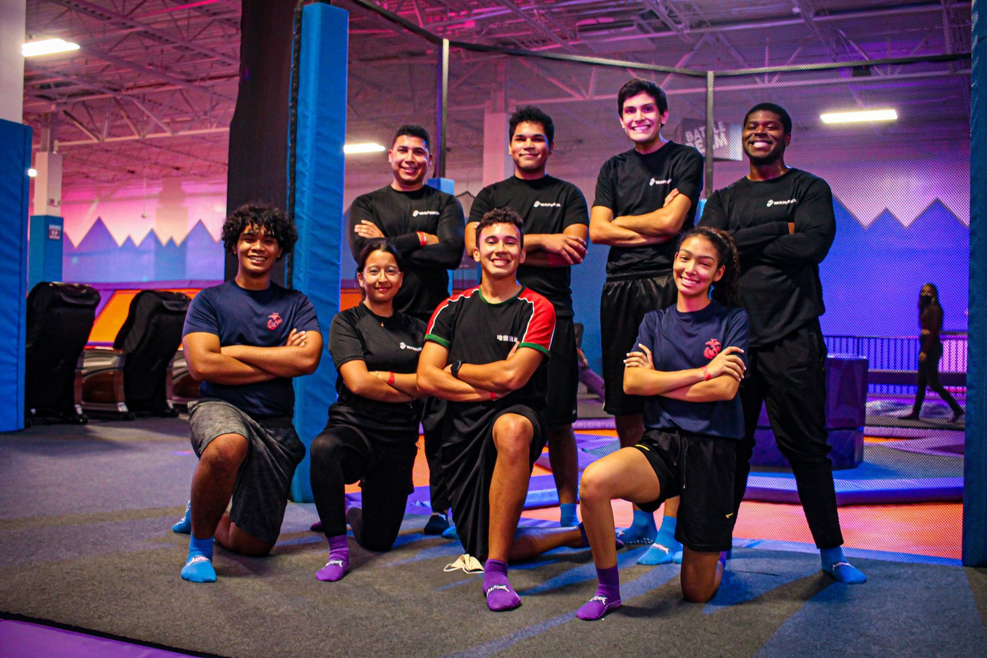Group of trampoline park staff, arms crossed, smiling. Indoor setting, purple and blue accents.