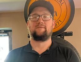 A man with a beard and glasses is standing in front of a tire.