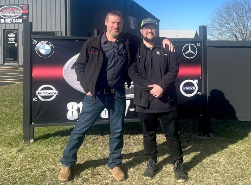 Two men are standing next to each other in front of a sign.