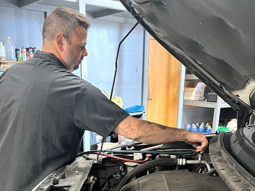 A man is working on the engine of a car with the hood open.