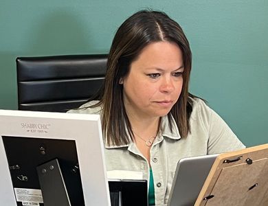 A woman is sitting at a desk looking at a tablet.