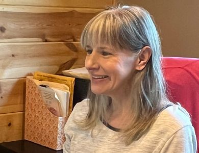 A woman is smiling while sitting at a desk in front of a wooden wall.