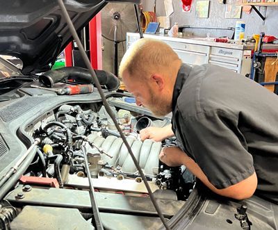 A man is working on the engine of a car in a garage.