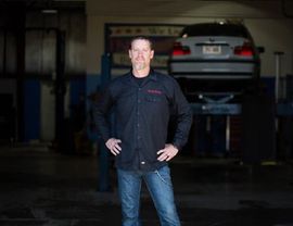 A man is standing in front of a car in a garage.