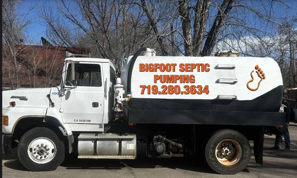 A septic tank truck with a shiny silver tank, green hose, and flashing red lights at night.