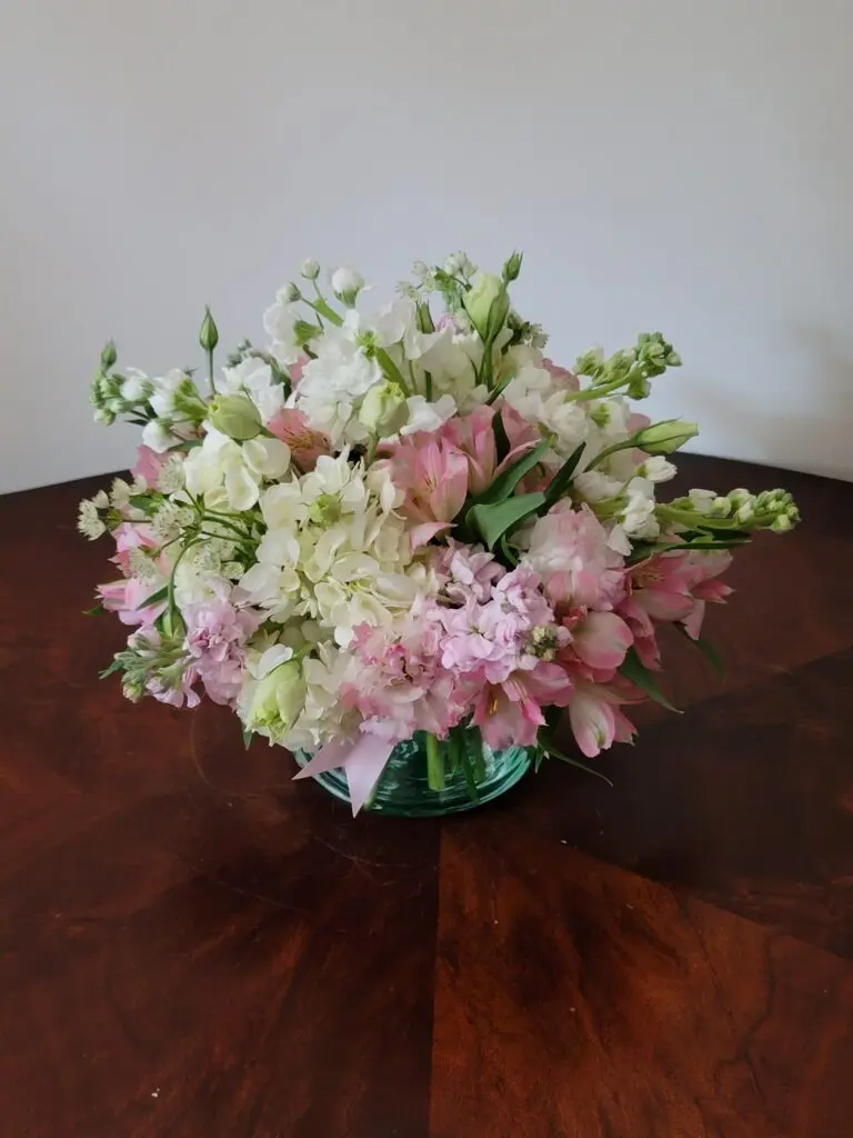 A vase filled with pink and white flowers is sitting on a wooden table.