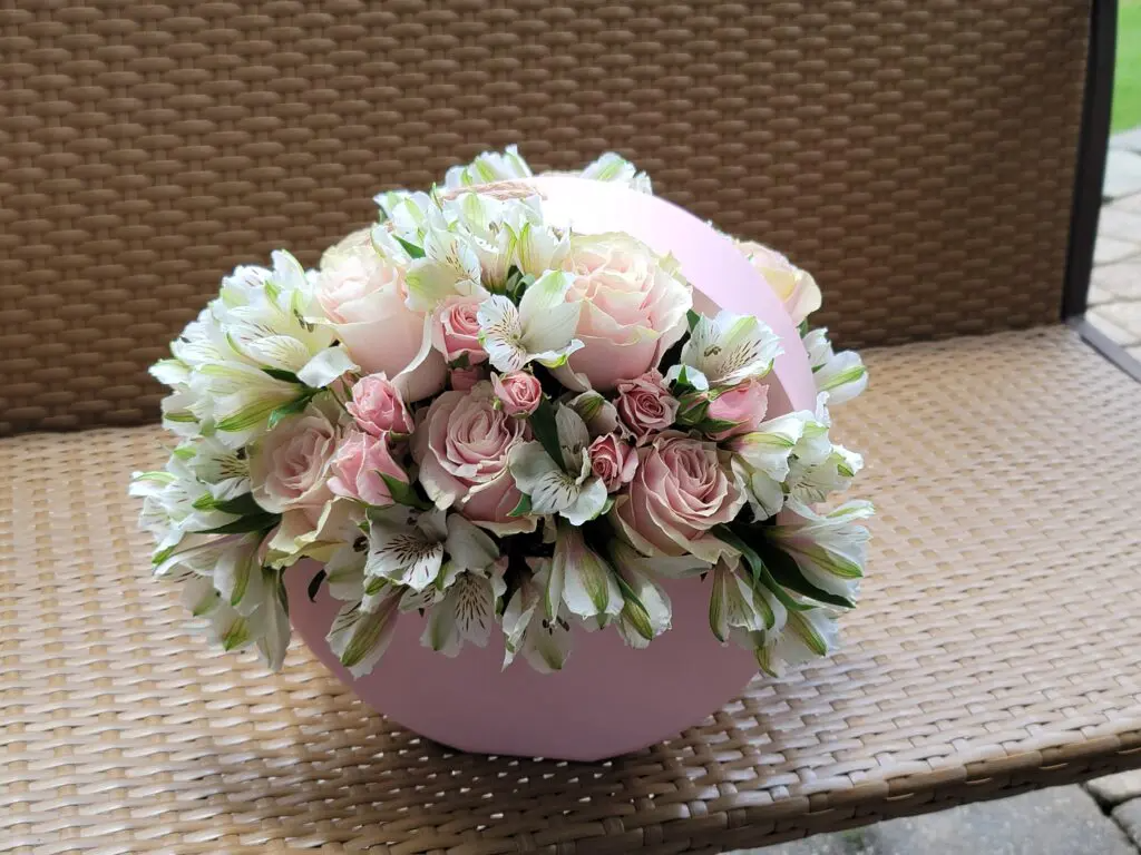A pink vase filled with pink and white flowers is sitting on a wicker chair.