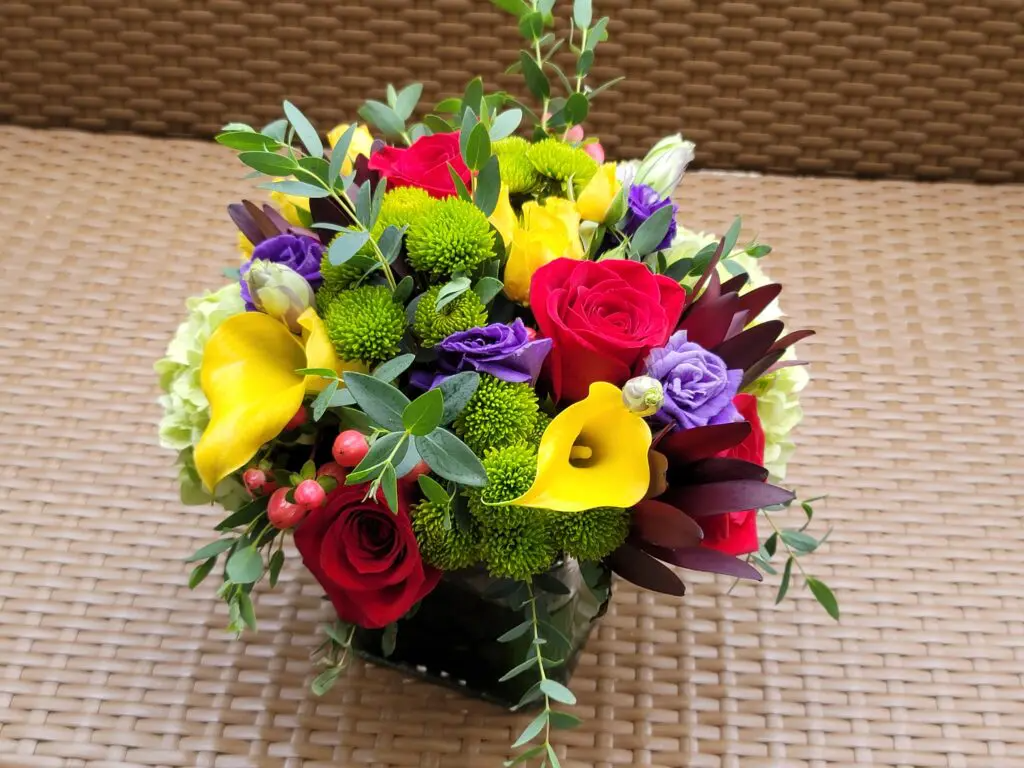 A vase filled with colorful flowers is sitting on a wicker table.