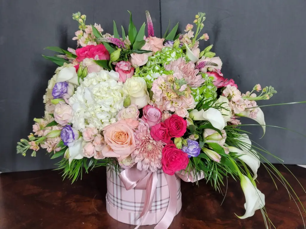 A pink box filled with flowers is sitting on a wooden table.