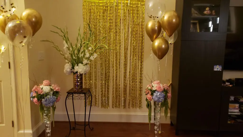A room decorated with balloons , flowers , and a gold curtain.