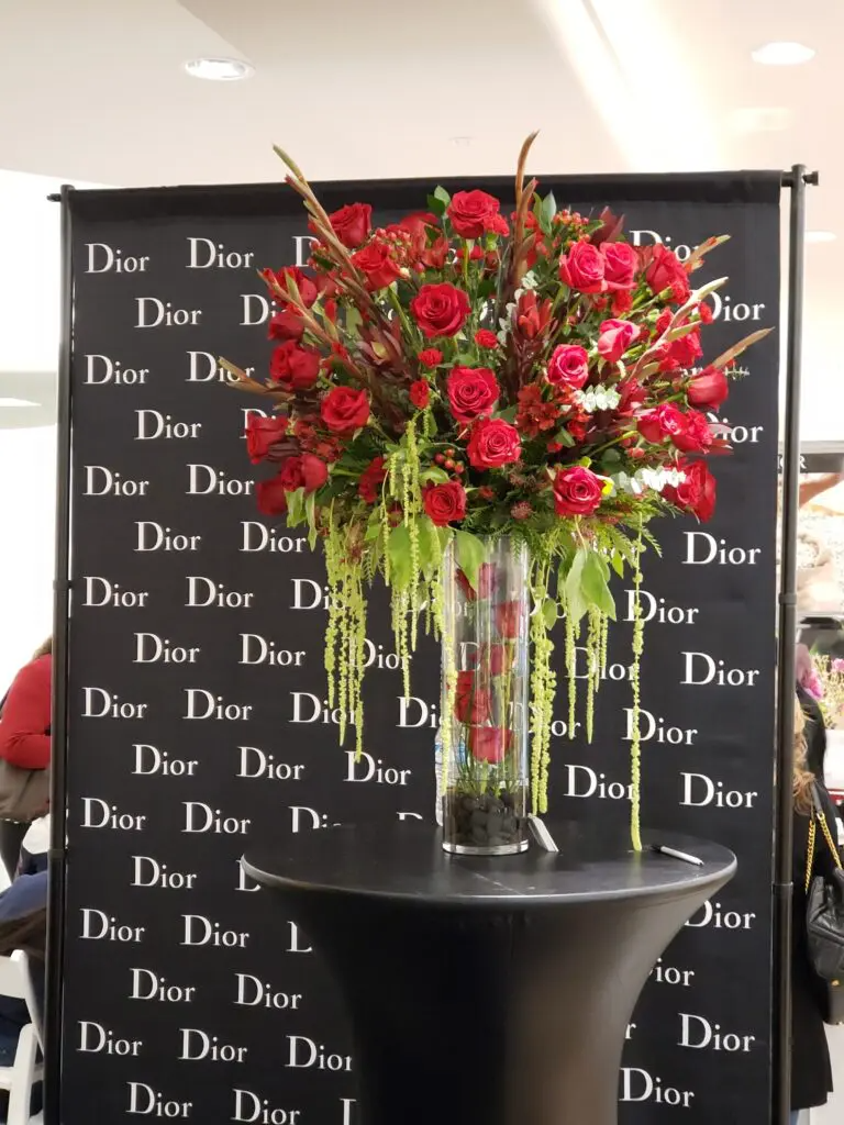 A vase filled with red roses sits in front of a dior sign