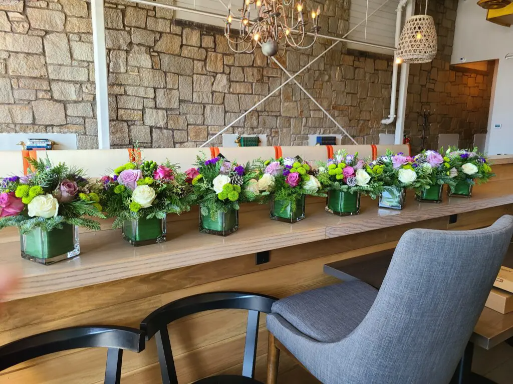 A row of vases filled with flowers are sitting on a wooden table.