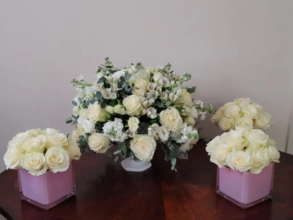 Three vases filled with white roses are sitting on a wooden table.