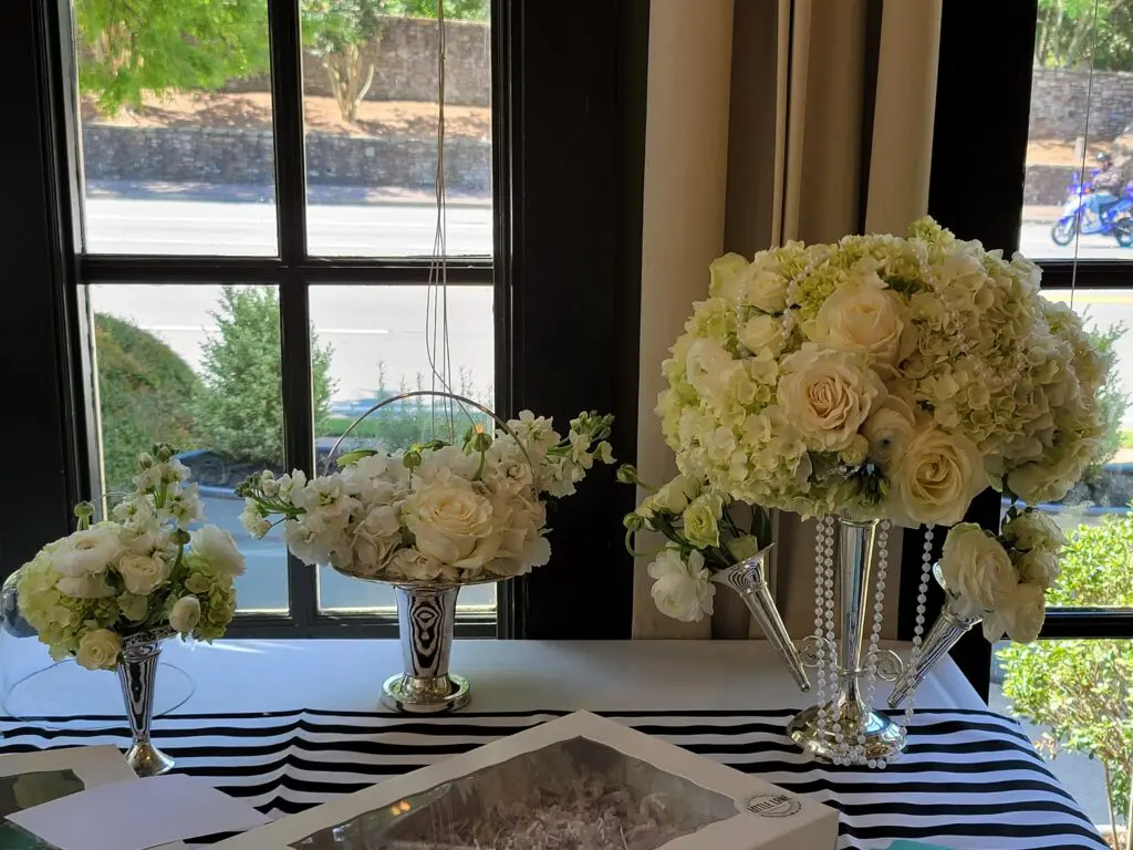 A table with white flowers in vases on it in front of a window.