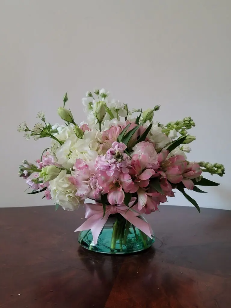 A vase filled with pink and white flowers is sitting on a wooden table.