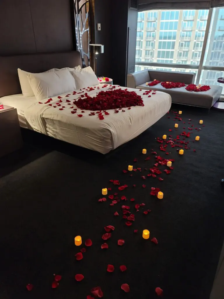 A hotel room with a bed decorated with rose petals and candles.