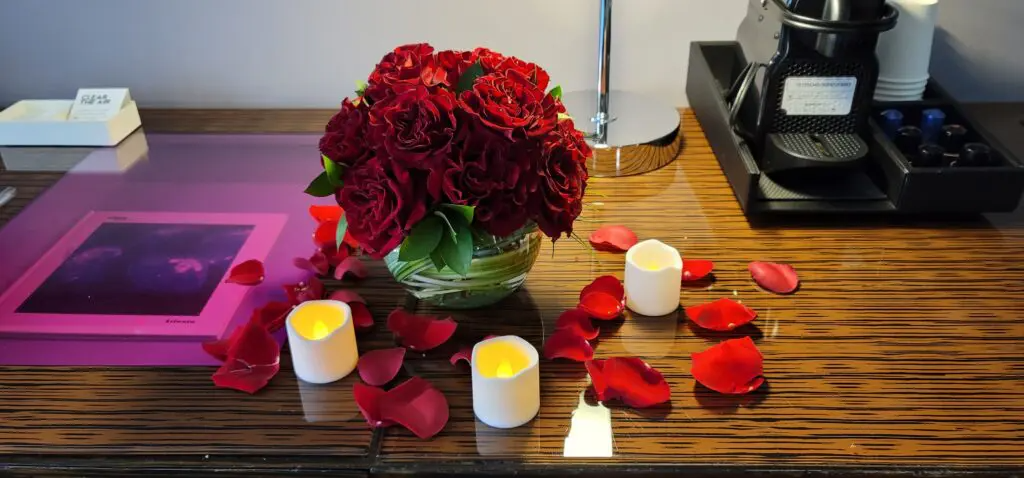 A table with a vase of red roses and candles on it.