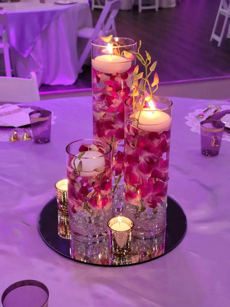 A table with three vases filled with flowers and candles on it.