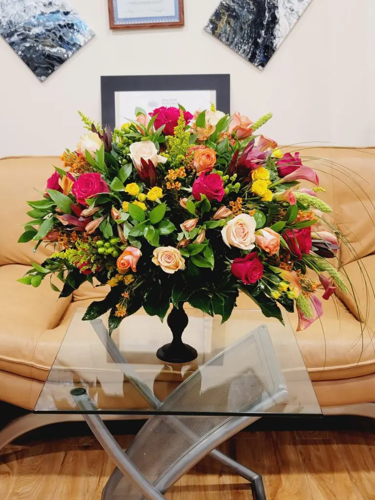 A vase of flowers sits on a glass table in front of a couch.