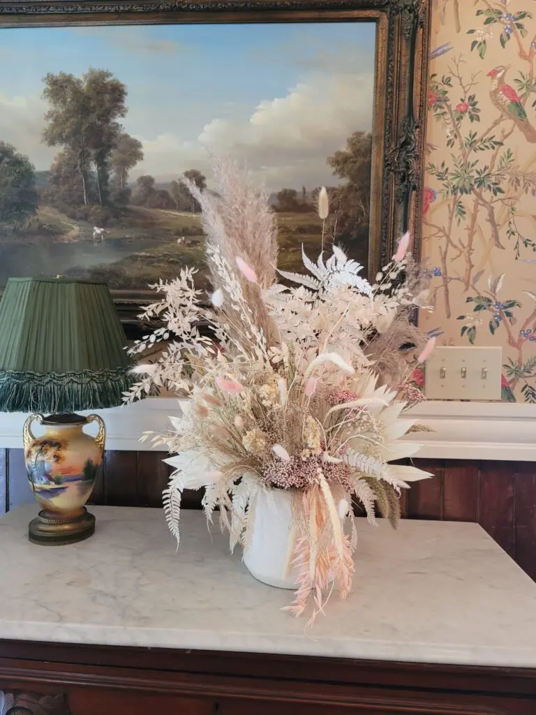 A vase filled with dried flowers is sitting on a table in front of a painting.
