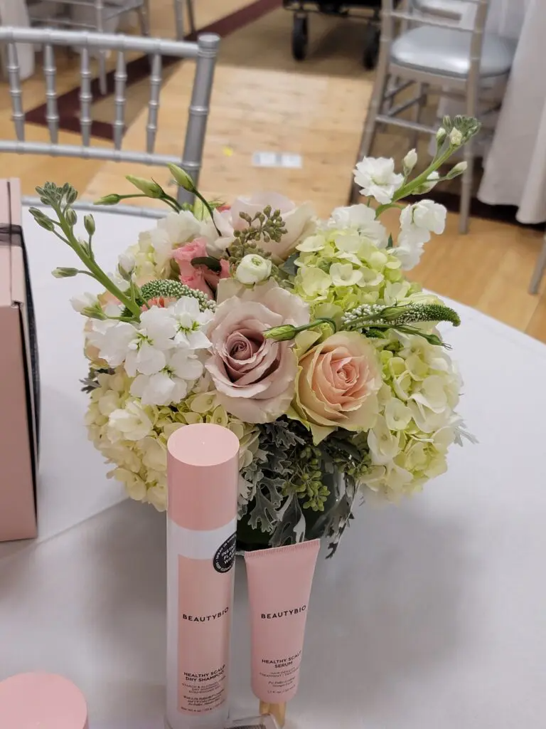 A table with a vase of flowers and two bottles of lotion on it.