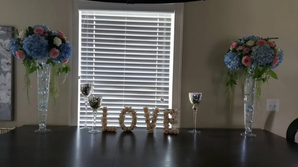 A table with two vases of flowers and a sign that says `` love '' in front of a window.