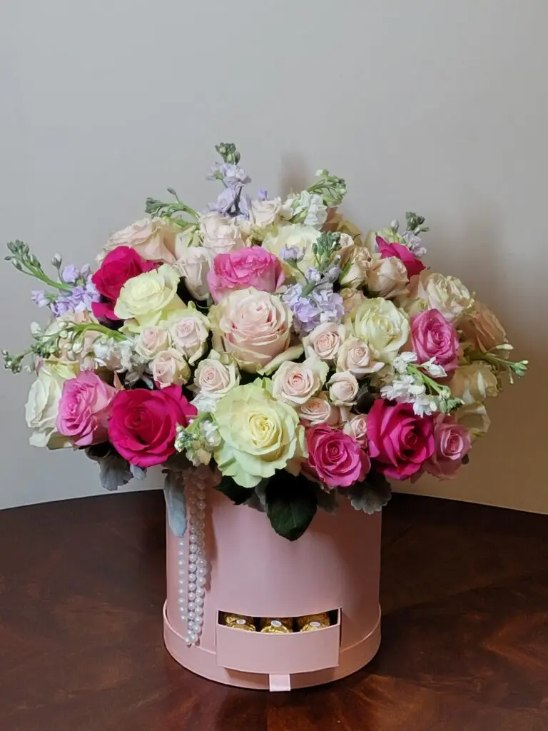 A pink box filled with flowers and chocolates on a wooden table.
