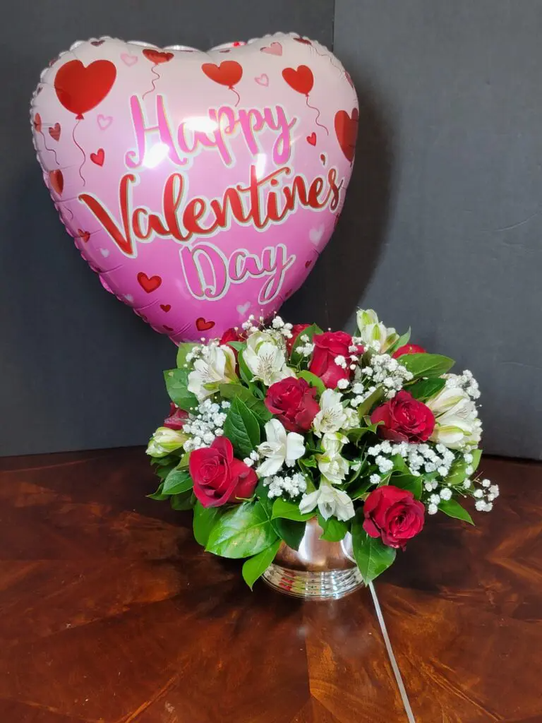 A happy valentine 's day balloon is sitting next to a vase of flowers.