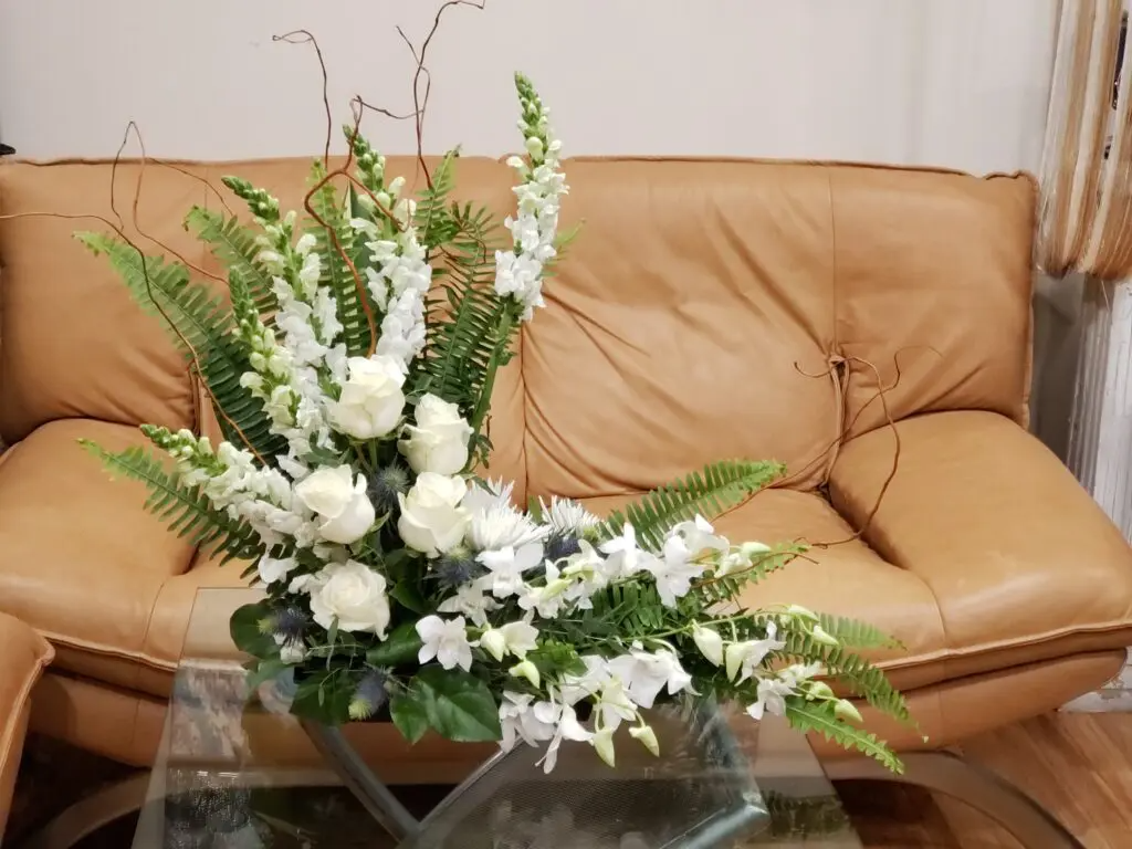 A vase of white flowers sits on a glass table in front of a couch.